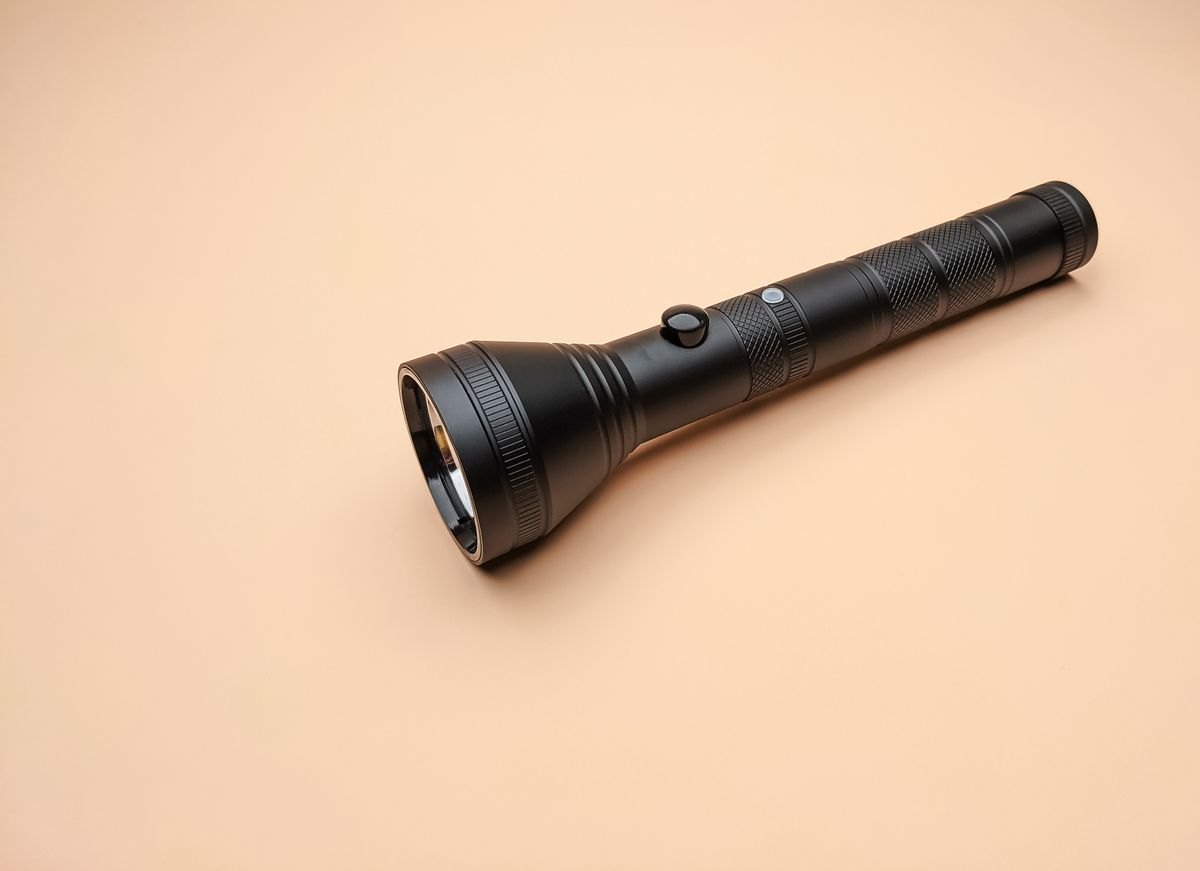 Black handheld flashlight lying on a plain surface