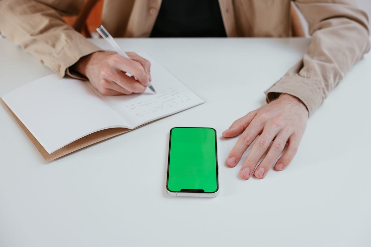 Person writing notes beside a phone