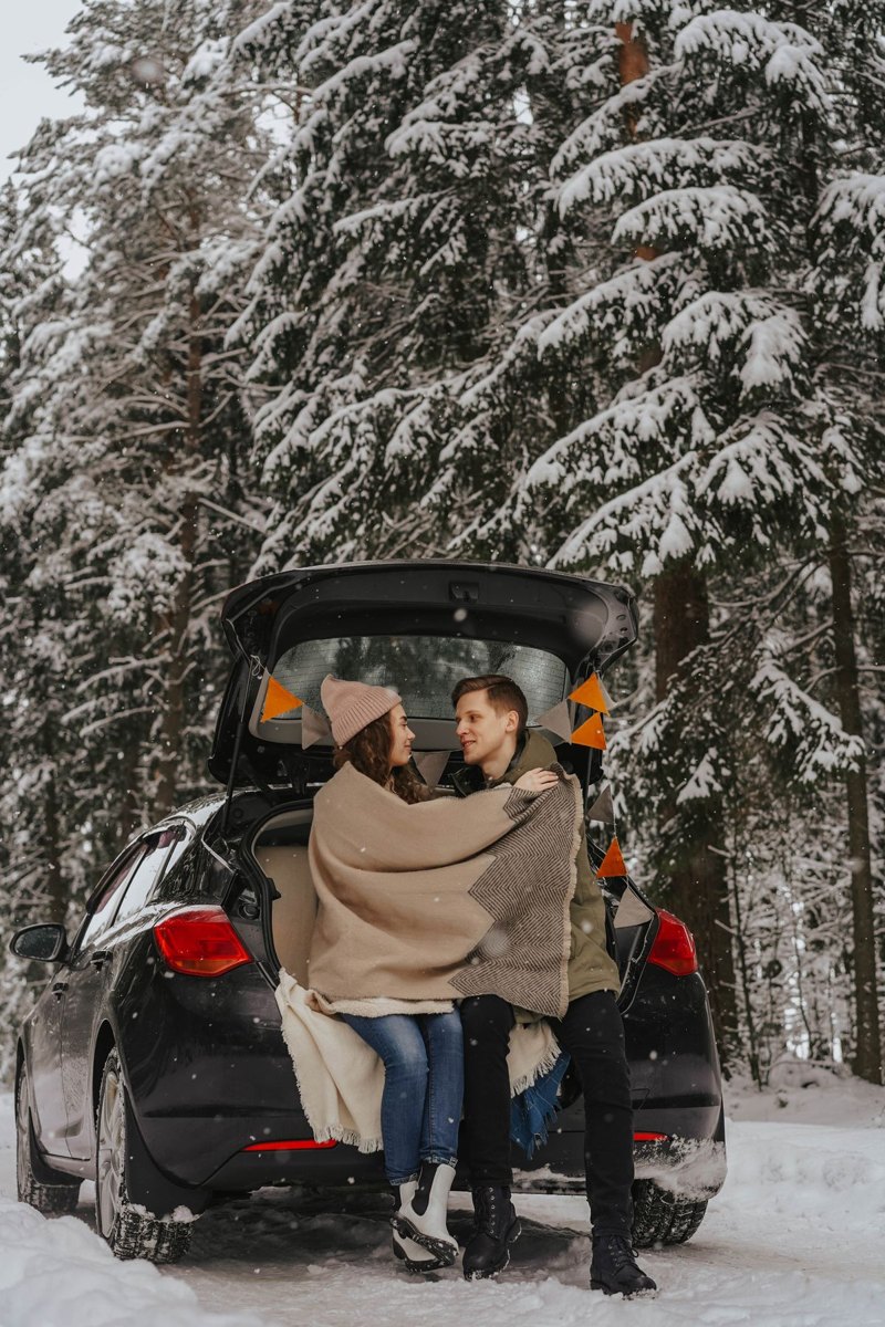 Two travelers sitting beside a car in a snowy setting